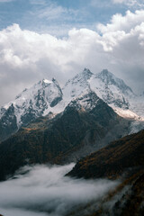 View of the valley and autumn foggy forest with snow covered mountain peaks
