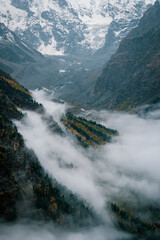 View of the valley and autumn foggy forest with snow covered mountain peaks