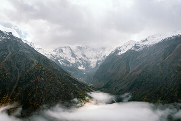 View of the valley and autumn foggy forest with snow covered mountain peaks