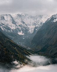 View of the valley and autumn foggy forest with snow covered mountain peaks