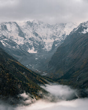 View of the valley and autumn foggy forest with snow covered mountain peaks
