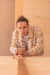 Handy man flattening wood plank with jack plane. Happy male woodworker looking at camera and...