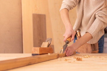 Person gouging wood with chisel. Top view of body part of anonymous carpenter carving wood on plank with chisel on workbench