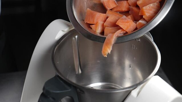 Chef putting pieces of fish into professional mincing machine in modern foodstuff manufacturing. Electric mincer Machine In Action. Slow motion. Salmon is cut into small pieces in food processor. full