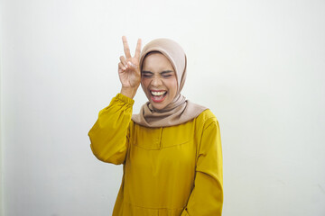 Cheerful muslim girl in hijab showing peace gesture and posing to camera studio background with free space