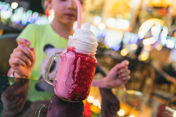 strawberry milkshake in a beautiful glass in a cafe. a child drinks a milkshake