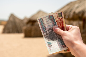 Egyptian pounds in a man's hand on the background of the beach. Egyptian money - obrazy, fototapety, plakaty