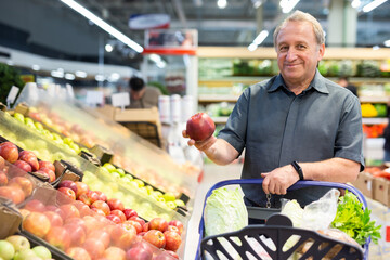 elderly man chooses apples in vegetable and fruit department