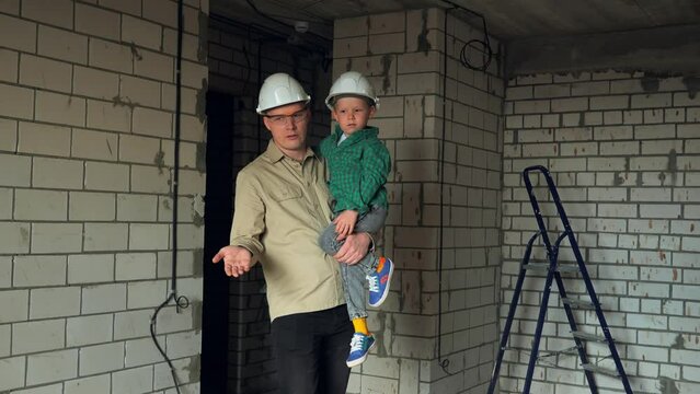 A father holds his son in his arms in the middle of a construction site and shows his future nursery. Father and son dream of what a children's room will look like. High quality 4k footage