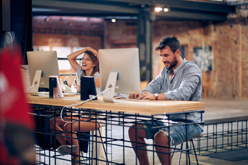 Two young workers, working in modern office in front of desktop computers.