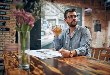 Man with glasses in cafe with newspaper and drink, looking in distance, thinking.