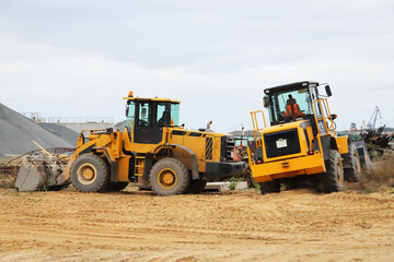 Two yellow heavy wheeled tractors bulldozers in the construction sand area
