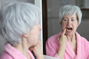 Senior woman opening her mouth in the mirror to observe her dental health 