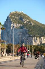 happy senior woman cycling with her electric mountain bike below the Rock of Gibraltar, Andalusia, Spain