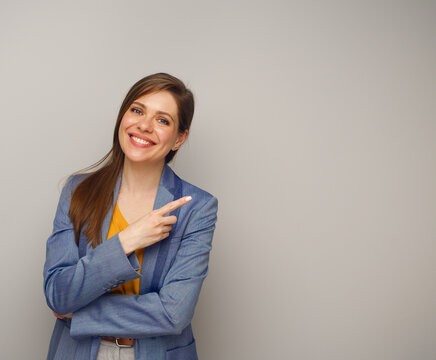 Smiling woman in blue business suit pointing finger at side, isolated female portrait.