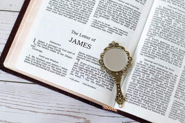 Open holy bible book of James with ancient golden mirror on wooden table. Top view. Biblical concept of Christian reflection, change, growth, obedience and liberty of the Law of God.