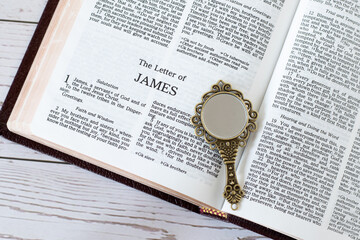 Open holy bible book of James with ancient golden mirror on wooden table. Top view. Biblical...