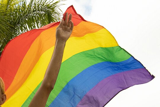Human hand holding LGBT flag in background of blue sky