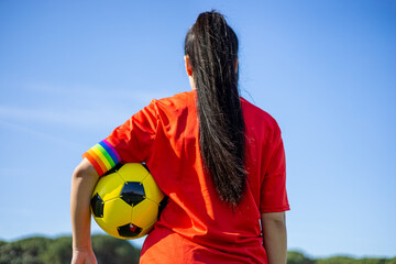 Soccer player woman with a soccer ball and captain armband with the LGBT pride flag on the field. Campaign against homophobia in football. LGBTQ people in sport concept. Women's Football.