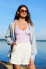 A young sexy woman in a shirt and shorts posing on the beach. Summer vacation by the sea