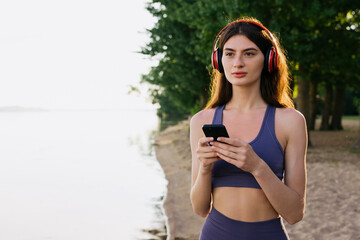 A young woman chooses music on her phone before jogging on the beach. The athlete trains outside