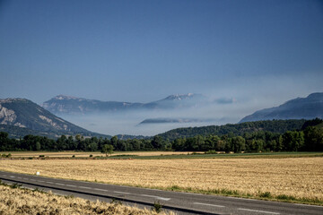Fototapeta premium Die, France - August 10th 2022 : Landscape representing a field of mowed wheat. In background, there is a mountain range. White smoke is that of a forest fire, caused by a flash during a thunderstorm