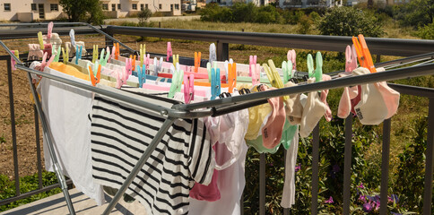 A clothes dryer with clothes and colorful clothes pegs stands drying things in the sun. Selective focus