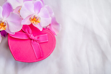 gift box in the form of heart and an orchid on white fabric 