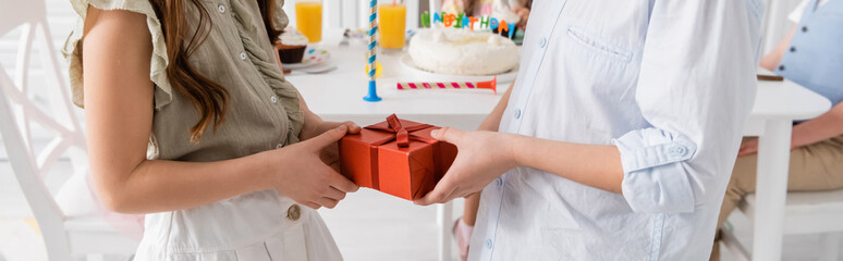 cropped view of preteen boy giving present to birthday girl near friends on blurred background, banner.