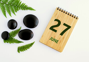 June 27. 27th day of the month, calendar date. Notepad, black SPA stoneJune s, green leaves. Summer month, day of the year concep