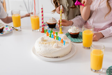 homemade birthday cake with candles next to cupcakes and glasses of orange juice.