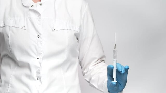 Close up shot of a doctor in blue medical gloves holding a syringe, pushing the plunger. 4k, slow motion.