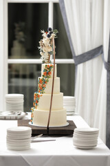 Four tiered ivory colored wedding cake on table at wedding reception.