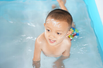 Hot weather. Boy playing with water happily in the tub.