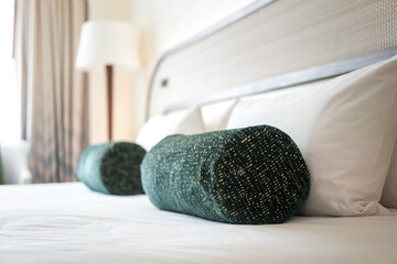 A green bolster cushion pillow is placed on the bed in luxury bed room. Interior decoration object photo, selective focus.