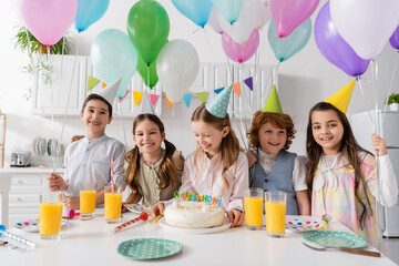 group of cheerful kids having fun during birthday party next to balloons at home.