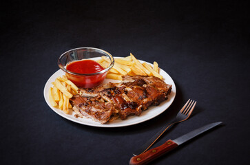 Baked pork ribs with french fries on white plate on dark background. Selective focus.