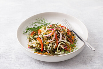 White plate with a salad of seaweed, white cabbage, carrots, sweet peppers, pickled red onions and herbs on a light gray background, top view. Healthy homemade food