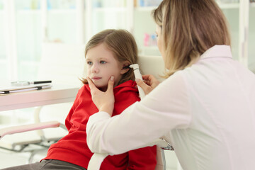 Caring doctor checks ears of girl with medical equipment