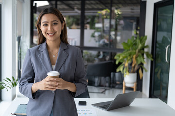 Young pretty businesswoman having a coffee break, smiling and holding a coffee cup in the office room.