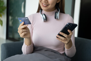 Pretty young woman shopping online with credit card and smartphone while siitng at her living room.