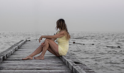 the lonely woman sitting on the old wooden jetty watches the sea