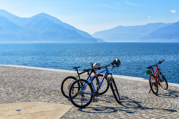 Tree bicycles on the Lago Maggiore promenade in Ascona, Switzerland with view to lake surrounded mountains - 592323621