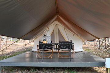 Large camping tent for luxurious outdoor getaway. White traditional tent with luxurious glamping interior with desk and black chair in forest, The concept of relaxing with nature on summer vacation.

