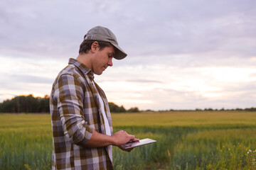 Farmer with a tablet computer in front of a sunset agricultural landscape. Countryside field. The concept of country life, food production, farming and technology concept.
