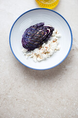 White plate with grilled red cabbage and feta cheese, top view on a beige stone background, vertical shot with copy space