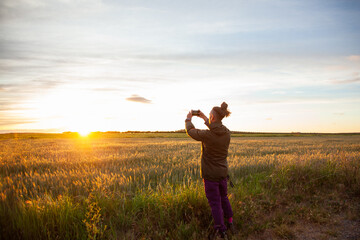 a boy from behind with long hair with a bow making photos with the mobile in the field looking at...