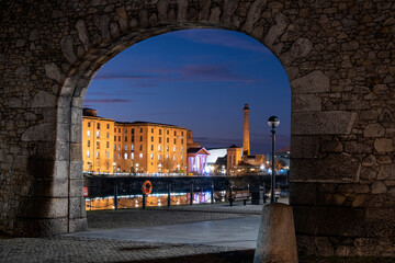 The Albert Dock and Pumphouse viewed through a remnant of the original dock wall at night, Liverpool Waterfront, Liverpool, Merseyside