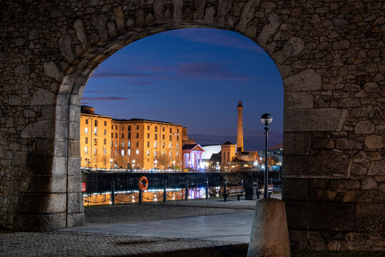 The Albert Dock and Pumphouse viewed through a remnant of the original dock wall at night, Liverpool Waterfront, Liverpool, Merseyside