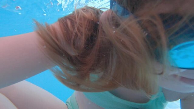 a kid girl wearing swimming goggles dives in the pool and takes a picture of himself.